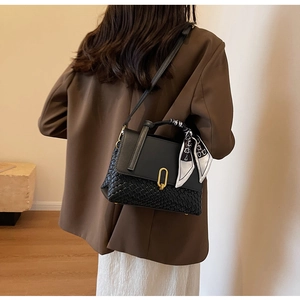Detail of woven black leather handbag with decorative silk scarf and gold U-shaped clasp