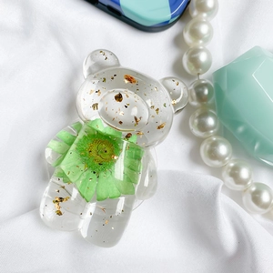 Detail of bear-shaped phone grip with embedded gold foil and green dried flower