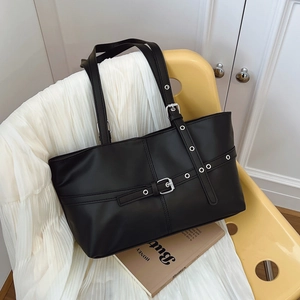 Retro black large tote bag with silver eyelets and buckle straps on a yellow chair