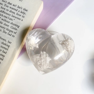 Makroansicht der klaren Herz-Handyhalterung mit weißem Glitzer auf einem Buchhintergrund