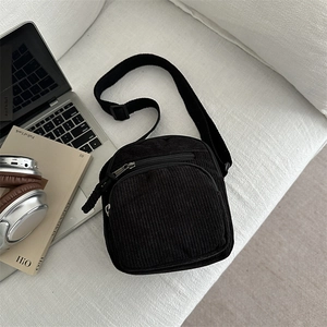 Minimalist black corduroy crossbody bag with silver zippers shown in a lifestyle flat lay