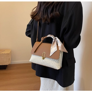 Detail of a two-tone woven handbag with gold U-buckle and silk scarf on the handle
