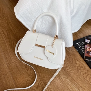 White leather saddle bag with metal trim and gold logo on light wood background