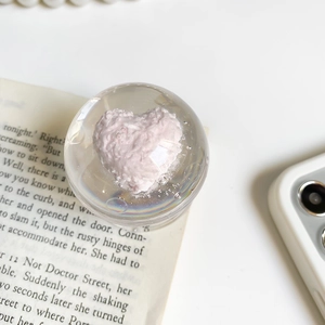 Vue détaillée du support téléphone sphérique transparent avec un coeur rose et nacré