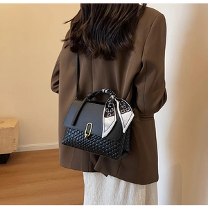 Detail of a chic handbag featuring black leather flap, woven texture, and silk scarf wrap
