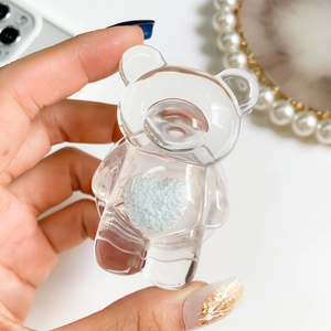 Transparent bear phone grip with blue velvet heart insert shown in hand for scale