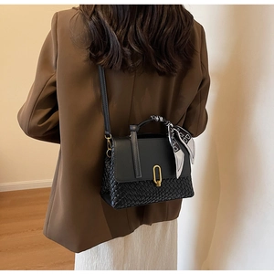 Detail of black woven leather handbag with gold lock and silk scarf worn by a model