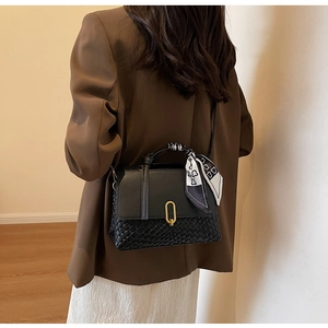 Detail of black woven handbag featuring a gold oval clasp and decorative silk scarf handle