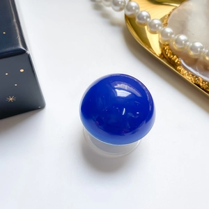 Close-up of a glossy deep blue spherical phone grip with a transparent base on a desk