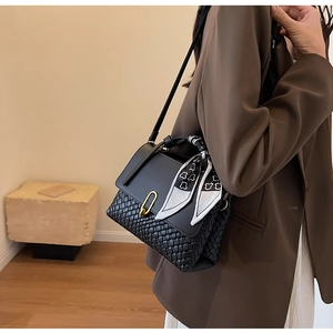 Detail of a black leather handbag with woven pattern, gold buckle and floral silk scarf