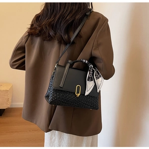 Detail of black woven crossbody bag with golden clasp and silk scarf wrapped on handle