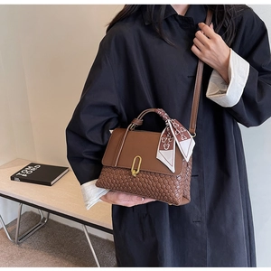 Detail of a brown textured woven handbag with gold buckle and a printed silk scarf accessory