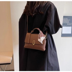 Detail view of brown woven handbag with silk scarf handle and gold U-shaped metal lock