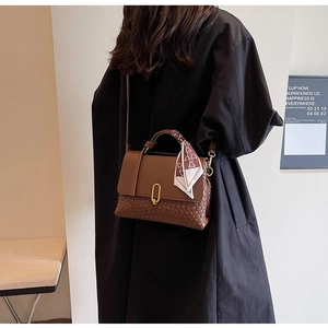 Close-up of brown textured leather handbag with gold buckle and scarf on a model
