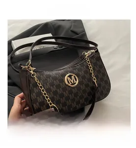 Dettaglio della borsa in pelle marrone scuro con motivo a lettere e logo M dorato su abito nero