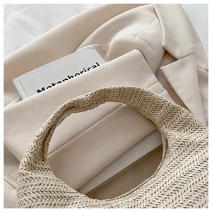 Detail of hand-woven straw hobo bag on beige blazer with elegant French minimalist aesthetic