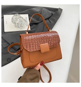 Detailansicht der karamellbraunen Handtasche mit Krokoprägung auf grauem Stoff drapiert