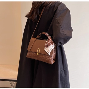 Detail of brown tote bag with woven texture, metal U-buckle and floral handle scarf