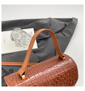 Detailansicht der braunen Krokodil-Textur und Goldbeschläge einer schicken Handtasche