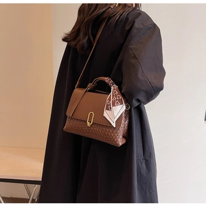 Detailed shot of brown leather handbag with woven texture, metal U-lock and silk scarf handle