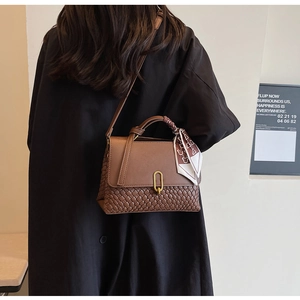 Detail of a brown textured crossbody bag featuring woven panels and a decorative silk scarf