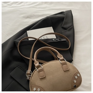 Detail of khaki suede satchel featuring silver rivets on black suit and white book