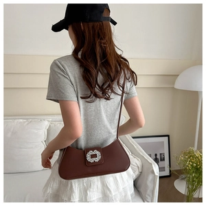 Detail view of a dark brown crescent underarm bag with a sparkling crystal buckle on model