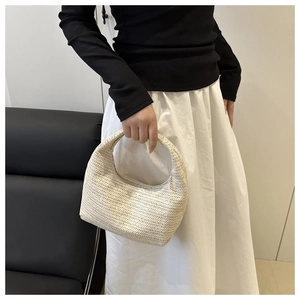 Detailed weave pattern of a beige woven hobo handbag held by a model in soft lighting