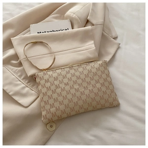Detail of beige monogram envelope bag with brown M pattern on a chic beige blazer background