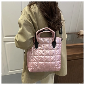 Pink quilted nylon puffer tote bag with black handles shown from a side view on a model