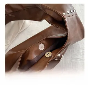 Close-up of silver magnetic clasp and rivet details on dark brown leather handbag