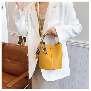 Detail of yellow lychee leather bucket bag with silk scarf and fashion logo plate