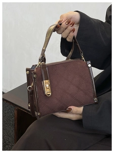 Detail of dark brown quilted suede handbag with gold lock and metal rivet trim
