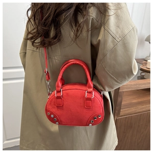 Red velvet retro pillow bag with silver rivets carried by a model in a beige outfit