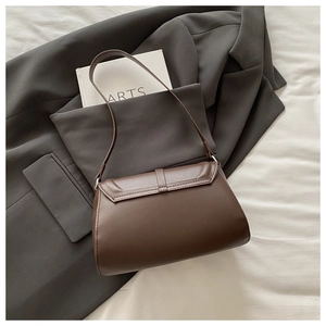 Flat lay of brown leather shoulder bag on white fabric with suit and arts book
