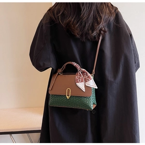 Detail of green woven handbag with brown leather flap and silk scarf handle decor