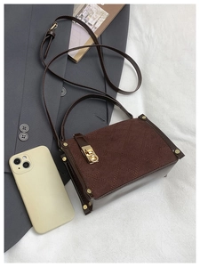 Close-up of brown quilted crossbody bag with vintage gold clasp on stylish grey fabric