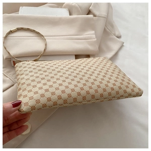 Close-up of beige envelope clutch bag with brown clover pattern and round wristlet strap
