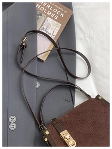Detail of dark brown quilted crossbody bag with gold metallic clasp on a stylish grey suit