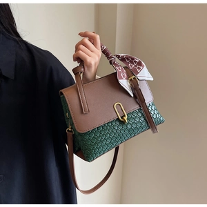Close-up of green woven handbag with brown leather flap and gold oval buckle detail