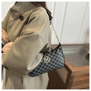Dettaglio borsa a tracolla vintage monogrammata con logo in oro su un trench-coat