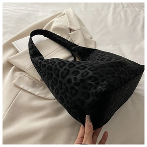 Detail of black leopard print hobo tote bag in plush texture over beige fabric background
