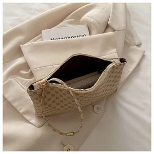 Detail of beige envelope bag showing red-brown monogram pattern and golden zipper