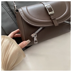 Detail of dark brown leather shoulder bag featuring silver metal buckles and decorative zippers