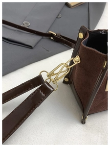 Close-up of contrast stitching and gold hardware on brown suede leather shoulder bag