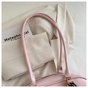 Detail of pink leather handbag with gold zipper and woven charm on a stylish blazer