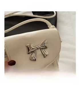 Detail of white leather shoulder bag with silver metal bow and tassel accents