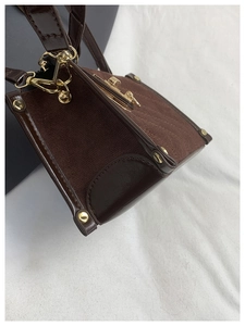 Detail of dark brown box-style mini crossbody bag with golden metal hardware and strap
