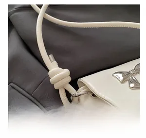 Close-up of white leather shoulder bag featuring silver bow buckle and fringe details