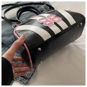 Detail of pink piping, metal studs and embroidered number on a striped crossbody bag